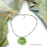 collier artisanal composé de perles dorées et vertes, orné d'un pendentif fleur en satin vert sur support en résine doré.