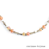 Gros plan sur l'enfilage du collier fait main montrant des perles facettées en verre orange et des perles hématites doré